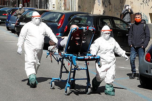 Медперсонал в полном защитном снаряжении перевозит пациента с подозрением на коронавирус по улице Неаполя. Транспортировка на машинах в Италии работает из рук вон плохо.