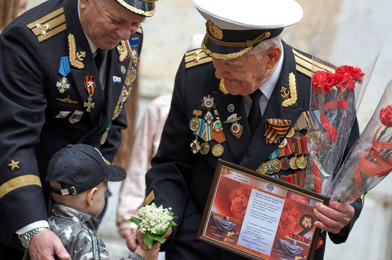 Ветеран Великой Отечественной войны, капитан 1-го ранга Лука Иванович Кузин (справа) принимает поздравления во время персонального парада во дворе своего дома в Севастополе.