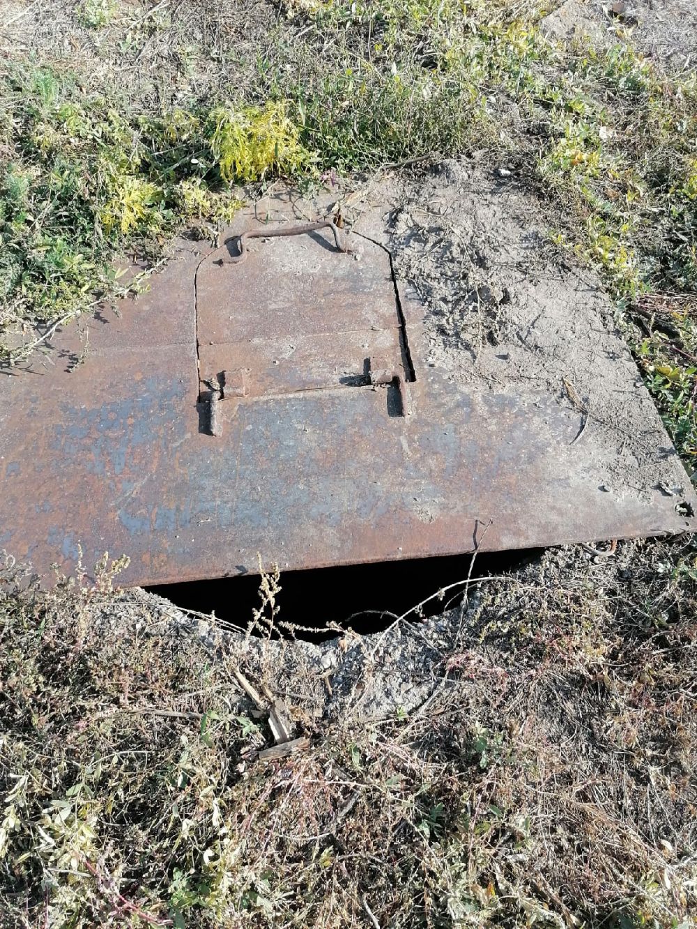На заднем дворе сливная яма прикрыта ржавым щитом.