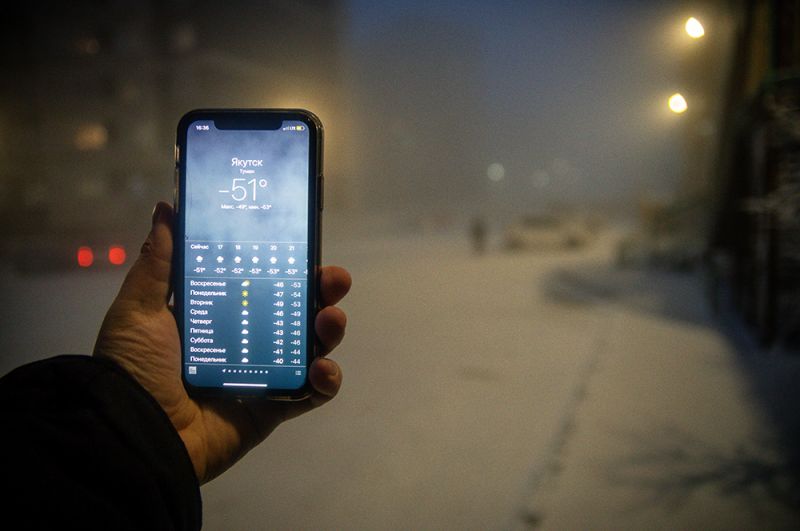 Мужчина демонстрирует мобильный телефон с информацией о прогнозе погоды.