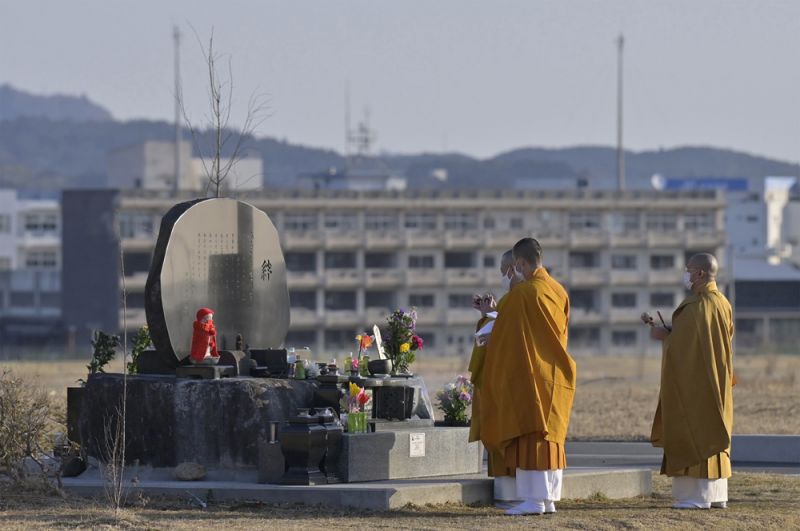 Буддийские монахи молятся перед мемориалом, воздвигнутым в память о жертвах землетрясения и цунами 11 марта 2011 года на фоне разрушенного цунами здания средней школы в Кесеннуме, на северо-востоке Японии,