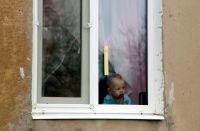 Маленький ребенок в окне одного из домов поселка шахты «Глубокая» в Горловке, который находится рядом с линией соприкосновения в Донецкой народной республике и постоянно подвергается обстрелам.