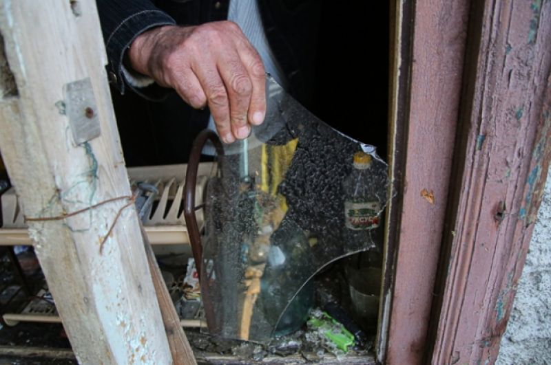 Местный житель из села Васильевка Донецкой области держит кусок разбитого стекла из разбитого окна жилого дома, пострадавшего в результате обстрела. 