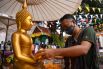 Мужчина в защитной маске поливает водой статую Будды.