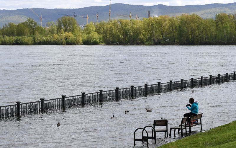 Девушка сидит на скамейке на затопленной набережной Енисея в центре Красноярска