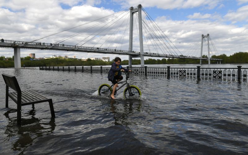 Ребёнок катается на велосипеде по затопленной набережной Енисея возле Виноградовского пешеходного моста в центре Красноярска