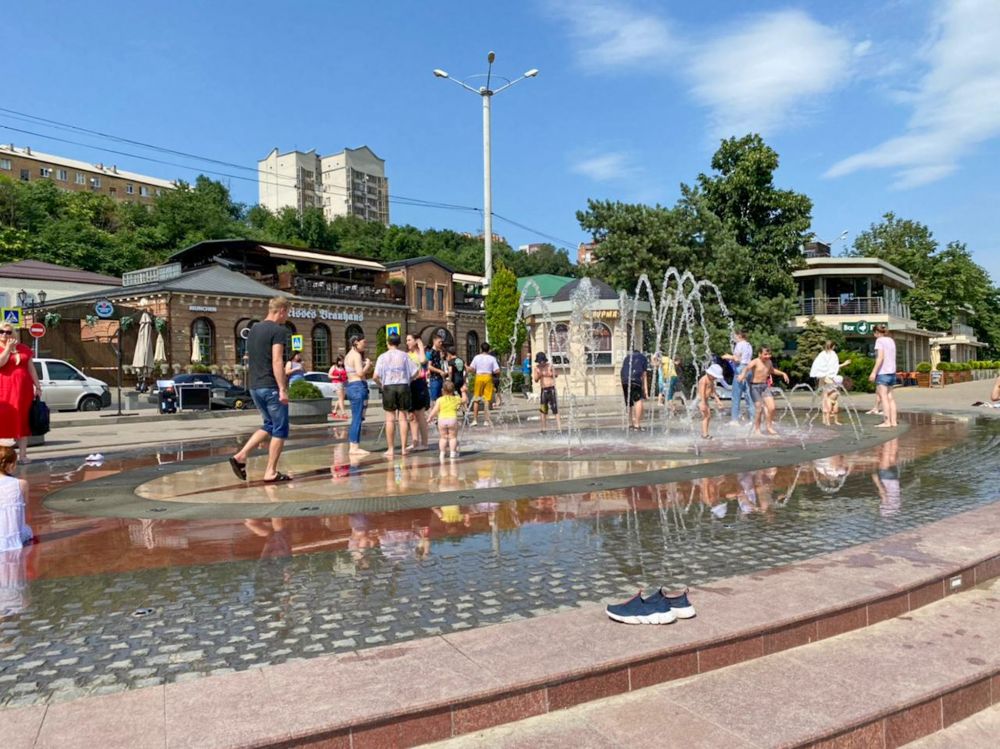 Взрослые и дети спасаются от жары в фонтане. Главное, не забыть кроссовки.