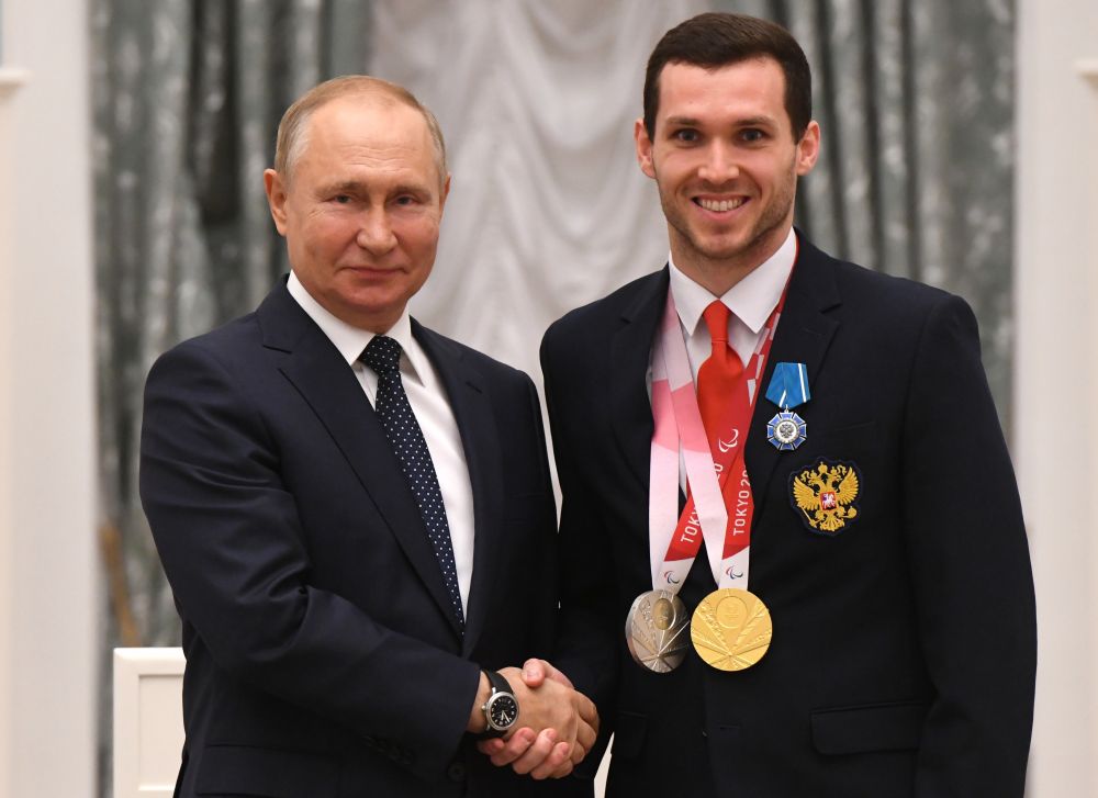 Президент РФ Владимир Путин и чемпион XVI Паралимпийских летних игр по плаванию спорта лиц с поражением опорно-двигательного аппарата в комбинированной мужской эстафете 4x100 м, серебряный призёр в дисциплине 50 м вольным стилем в классе S9 Денис Тарасов (справа) на церемонии вручения государственных наград РФ победителям XVI Паралимпийских летних игр 2020 года в Токио