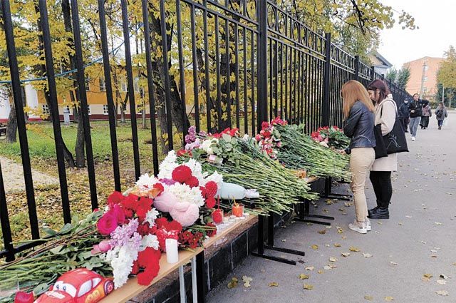 Люди несут цветы к стихийному мемориалу около ограды университета.  