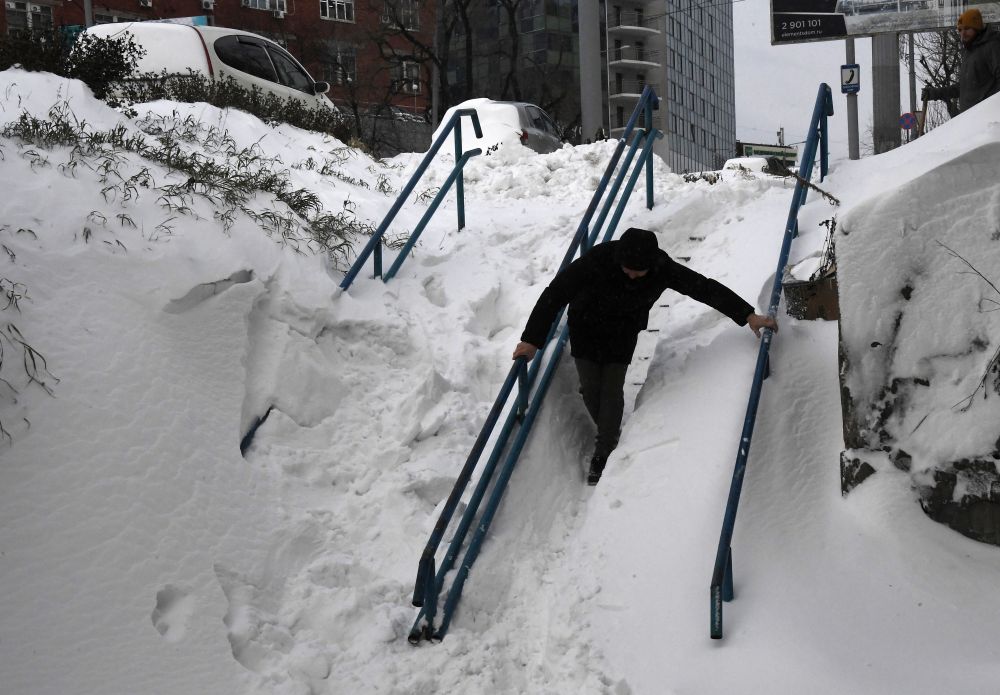 Мужчина идёт по заснеженной лестнице на проспекте Красного Знамени во Владивостоке после сильного снегопада