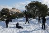 Молодые люди играют в снежки на холме Филопаппа в Афинах. На втором плане: храм Парфенон, расположенный в центральной части Акрополя