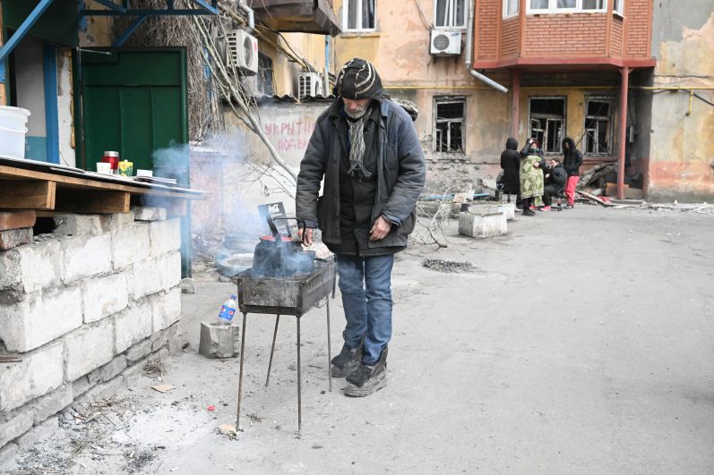 Мужчина готовит еду во дворе жилого дома в Мариуполе