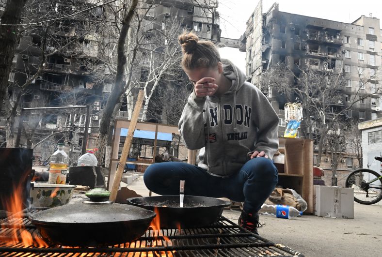 Жительница Мариуполя готовит еду во дворе разрушенного дома