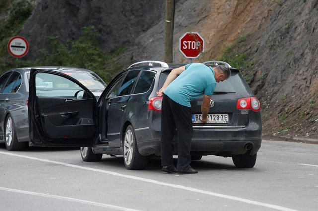 Водитель снимает наклейку, закрывающую национальную символику, с номерных знаков автомобиля на границе Сербии и Косово.