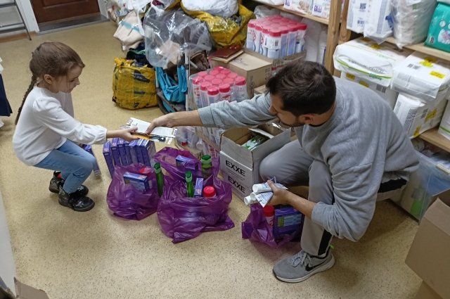 Маленькая помощница фонда и сотрудник Саша собирают гуманитарные наборы для пожилых беженцев.