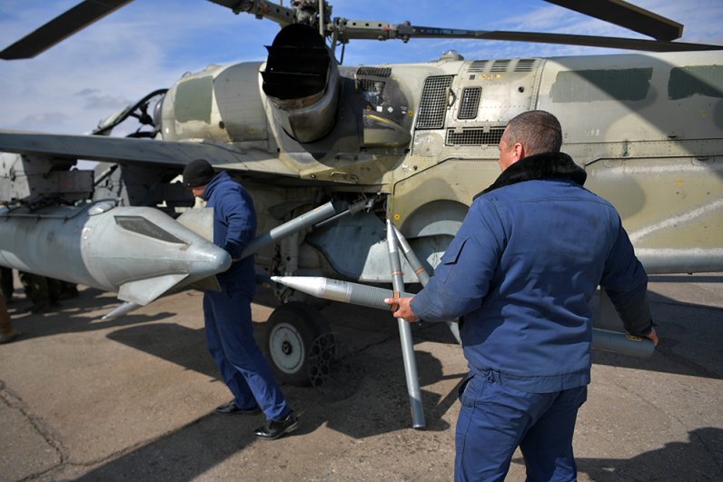 Технический персонал загружает неуправляемые авиационные ракеты (НАРы) в блок, установленный на вертолете Ка-52, перед боевым вылетом.