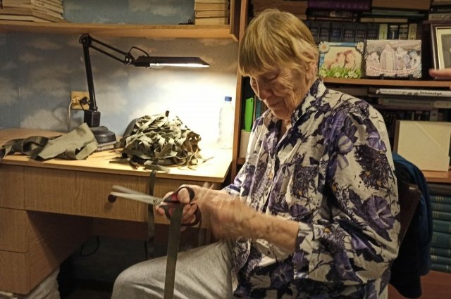 Учитель-пенсионер Тамара Галкина мастерски нарезает ленточки из ткани защитного цвета – основу маскировочных сетей и накидок для бойцов.