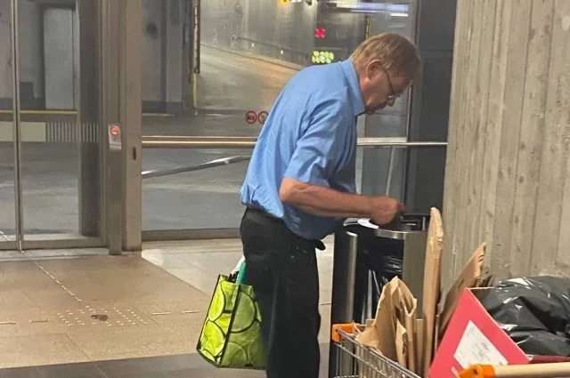 Пожилой мужчина ищет пустые бутылки в урне финского гипермаркета