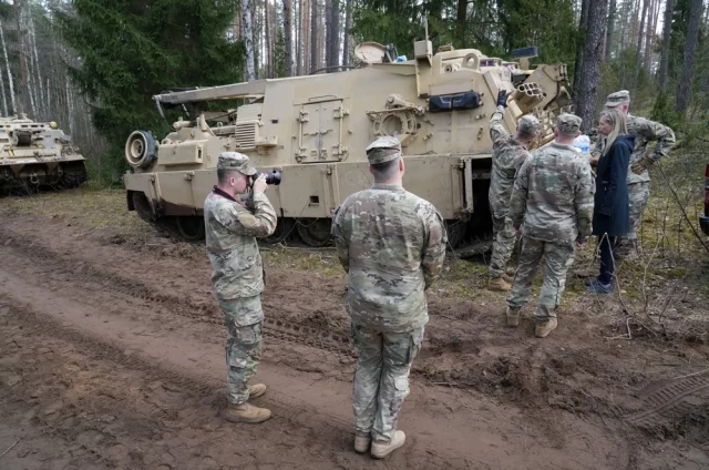 Посол США в Литве Кара К. Макдональд и военнослужащие армии США стоят возле бронированной ремонтно-эвакуационной машины M88 Hercules на месте спасательной операции на полигоне Пабраде.