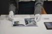 Посетительница в белых перчатках листает книгу, где собраны визуальные и текстовые материалы одного из представленных проектов. 