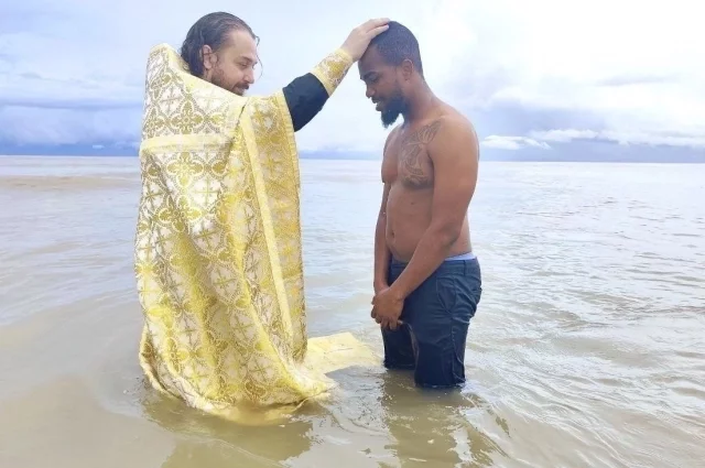 Отец Альвиан крестит африканского верующего в водах Индийского океана