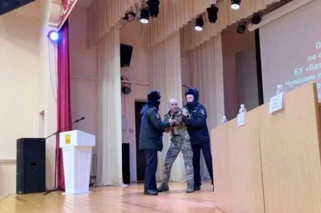 Сотрудники полиции пытаются увести участника СВО со сцены, лишая его возможности задать вопросы во время открытого обсуждения.