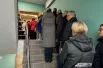 Люди стоят в длинной очереди, которая начинается с 1 этажа ДК. 