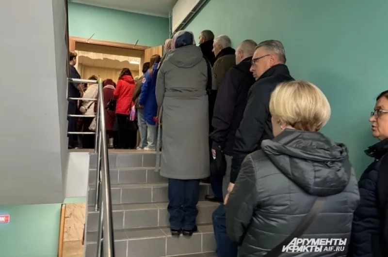 Люди стоят в длинной очереди, которая начинается с 1 этажа ДК. 