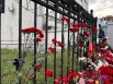 Некоторые из горожан привязывают гвоздики чёрными лентами к прутьям ограждения.